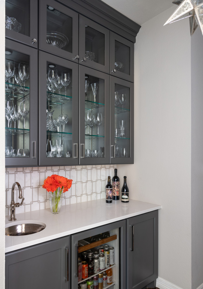 Photo of a transitional galley wet bar in Dallas with an undermount sink, grey cabinets, white splashback, medium hardwood floors, brown floor and white benchtop.