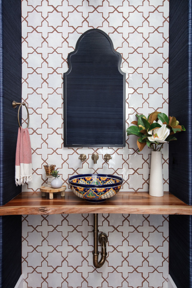 Small mediterranean powder room in San Diego with white tile, ceramic tile, blue walls, terra-cotta floors, a vessel sink, wood benchtops, brown floor, brown benchtops, a floating vanity and wallpaper.