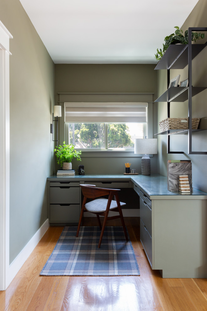Modelo de despacho tradicional renovado pequeño con paredes verdes, suelo de madera en tonos medios y escritorio empotrado