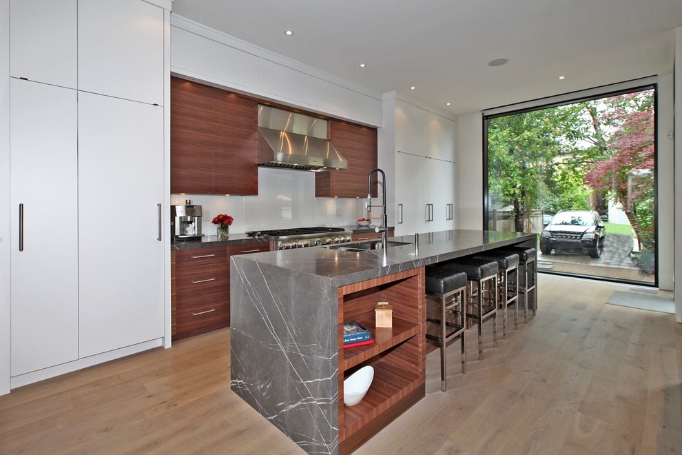 This is an example of a modern galley eat-in kitchen in Toronto with an undermount sink, flat-panel cabinets, white cabinets, white splashback, stainless steel appliances and marble benchtops.