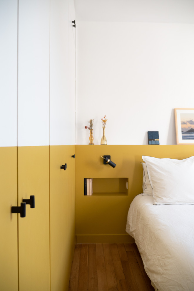 Cette image montre une chambre parentale minimaliste de taille moyenne avec un mur jaune, parquet clair, aucune cheminée et dressing.