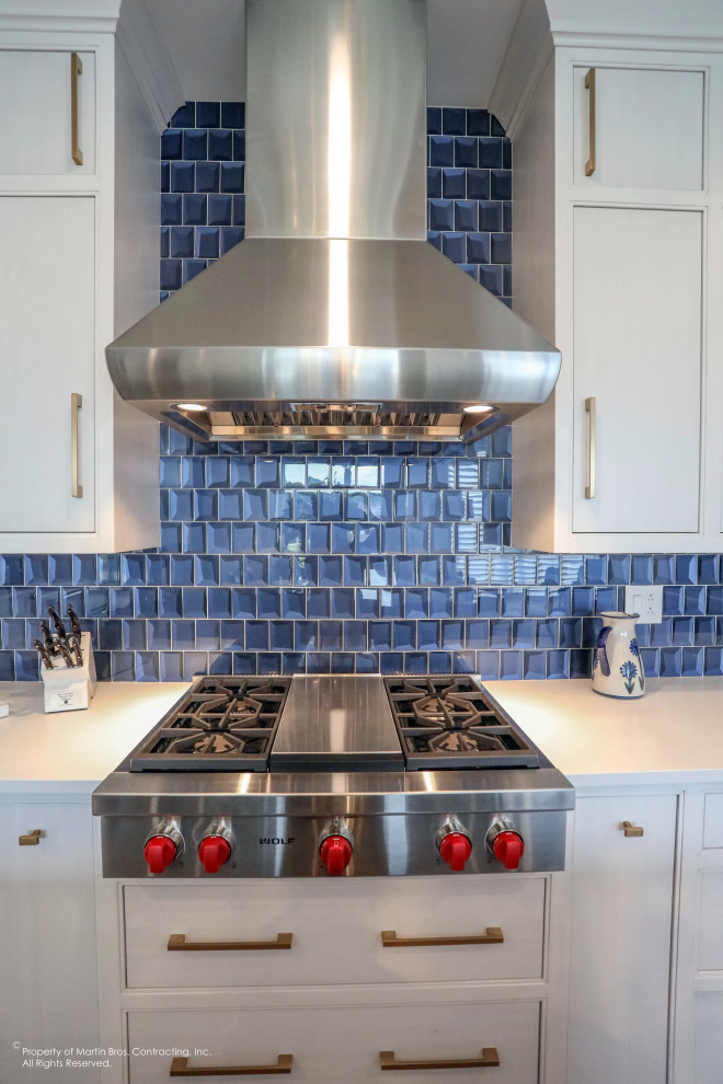 Open concept kitchen - mid-sized transitional u-shaped medium tone wood floor open concept kitchen idea with a single-bowl sink, flat-panel cabinets, white cabinets, quartz countertops, blue backsplash, glass tile backsplash, stainless steel appliances, an island and white countertops