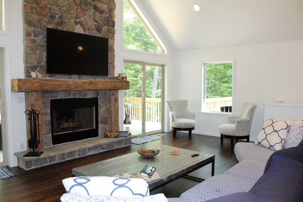 This is an example of a large country open concept living room in Other with white walls, dark hardwood floors, a standard fireplace, a stone fireplace surround, a wall-mounted tv and brown floor.