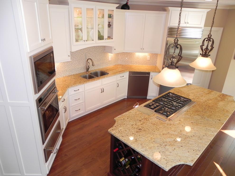Photo of a mid-sized traditional u-shaped open plan kitchen in Indianapolis with an undermount sink, shaker cabinets, white cabinets, granite benchtops, beige splashback, glass tile splashback, stainless steel appliances, medium hardwood floors, with island and brown floor.