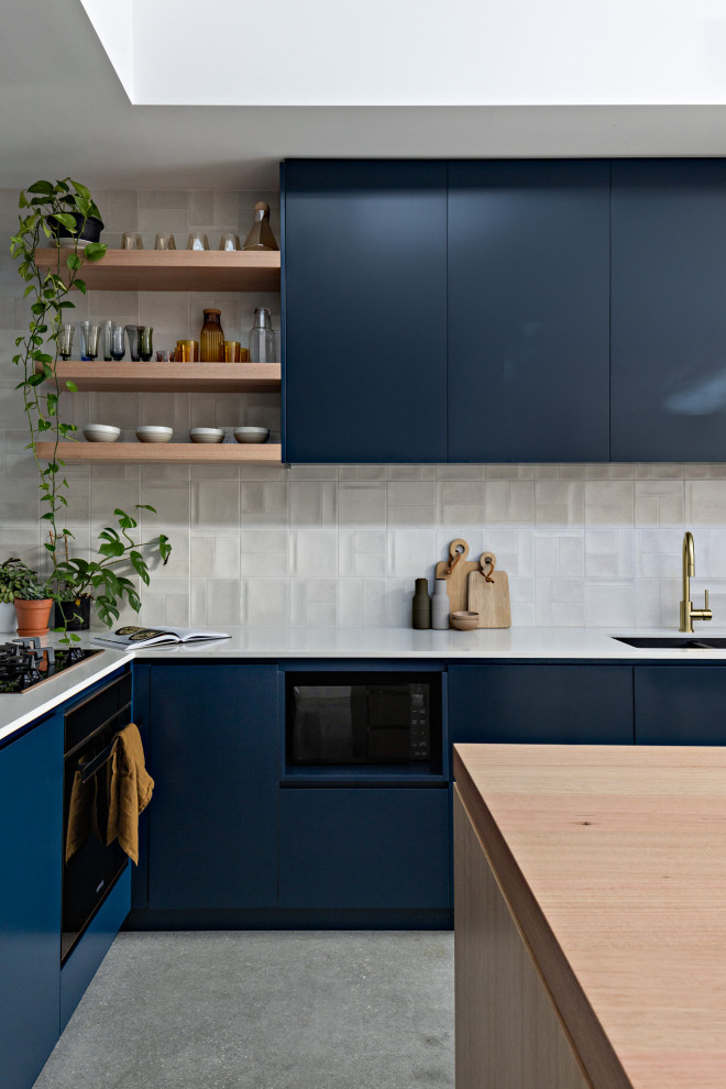 Esempio di una piccola cucina minimal con lavello sottopiano, ante blu, top in quarzo composito, paraspruzzi bianco, paraspruzzi con piastrelle in ceramica, elettrodomestici neri, pavimento in cemento, pavimento grigio e top bianco