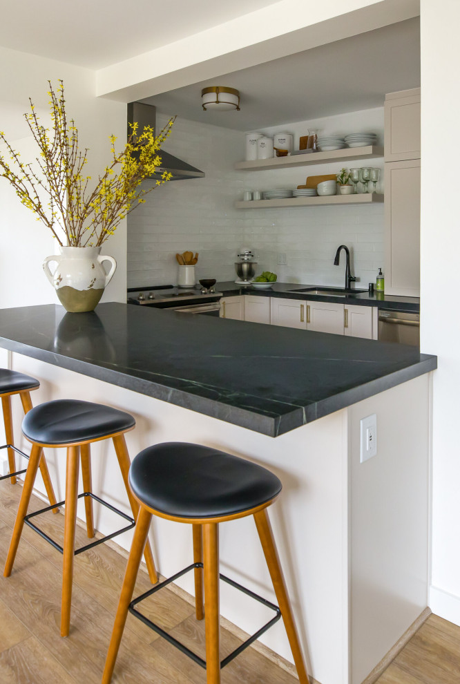Inspiration for a small modern u-shaped eat-in kitchen in Hawaii with a drop-in sink, shaker cabinets, white cabinets, soapstone benchtops, white splashback, subway tile splashback, stainless steel appliances, vinyl floors, with island, brown floor and black benchtop.