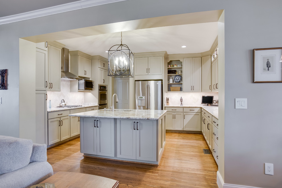 Inspiration for a transitional u-shaped medium tone wood floor and brown floor enclosed kitchen remodel in Birmingham with a double-bowl sink, shaker cabinets, beige cabinets, granite countertops, beige backsplash, travertine backsplash, stainless steel appliances and an island