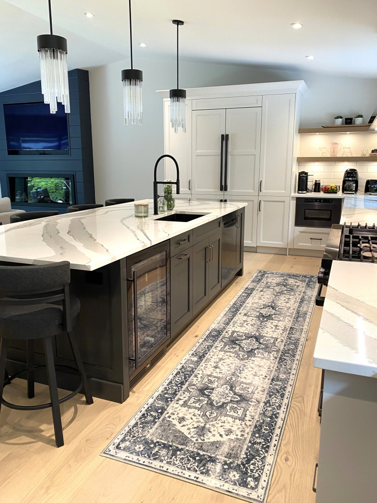 Open concept kitchen - large transitional l-shaped light wood floor and vaulted ceiling open concept kitchen idea in Toronto with an undermount sink, recessed-panel cabinets, white cabinets, quartz countertops, white backsplash, porcelain backsplash, stainless steel appliances, an island and white countertops