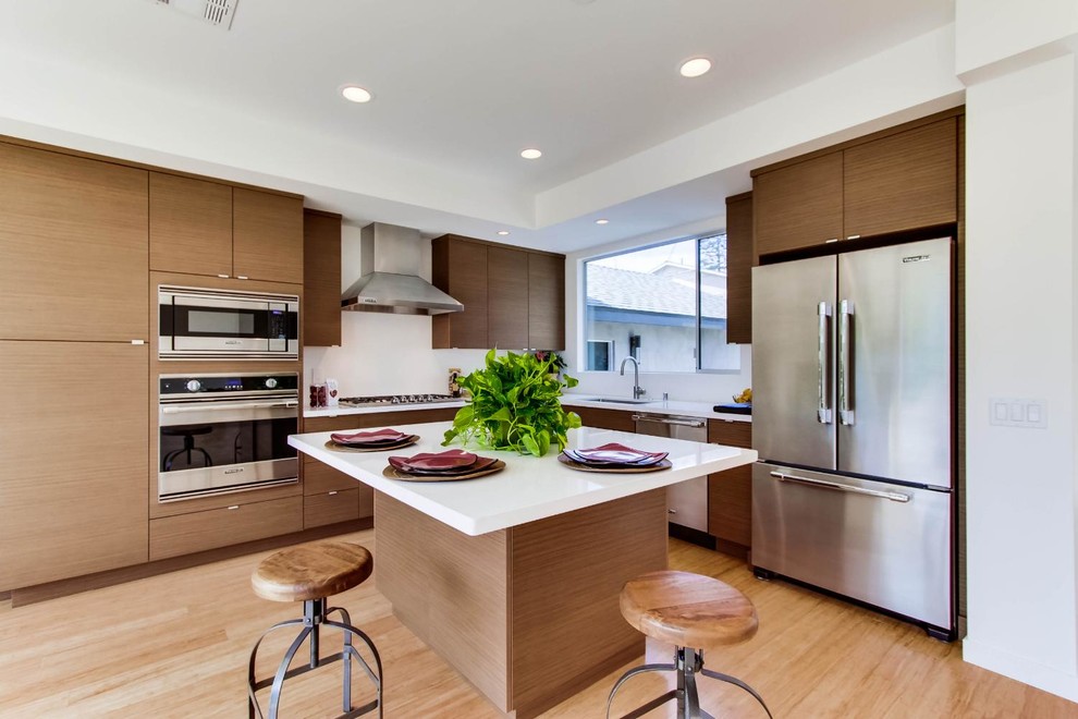 Large trendy l-shaped light wood floor eat-in kitchen photo with a double-bowl sink, flat-panel cabinets, medium tone wood cabinets, white backsplash, stainless steel appliances, white walls and an island