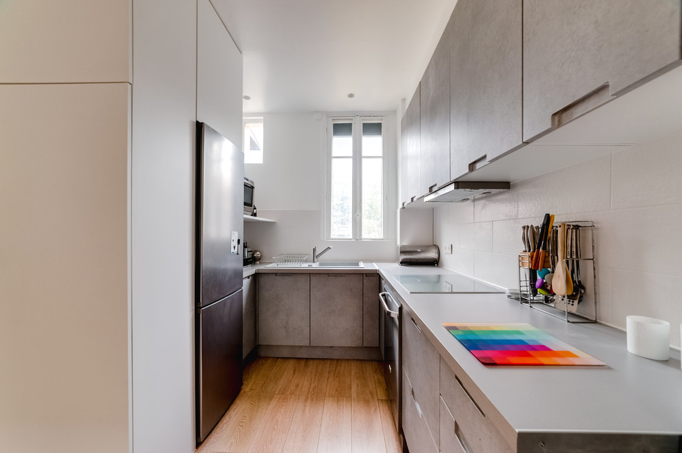 Exemple de cuisine ouverte in U With un évier encastré, un placard à porte plane, des portes de placard grises, un plan de travail en stratifié, une crédence blanche, une crédence en carreau de porcelaine, un électroménager en acier inoxydable, sol en stratifié, aucun îlot, un sol beige and un plan de travail gris.