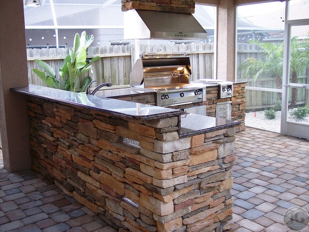 This is an example of a large traditional backyard patio in Tampa with an outdoor kitchen, no cover and concrete pavers.
