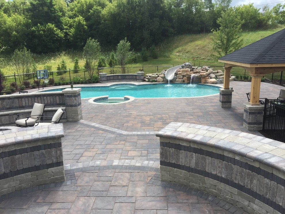 Photo of a transitional backyard custom-shaped pool in Detroit with a hot tub and brick pavers.
