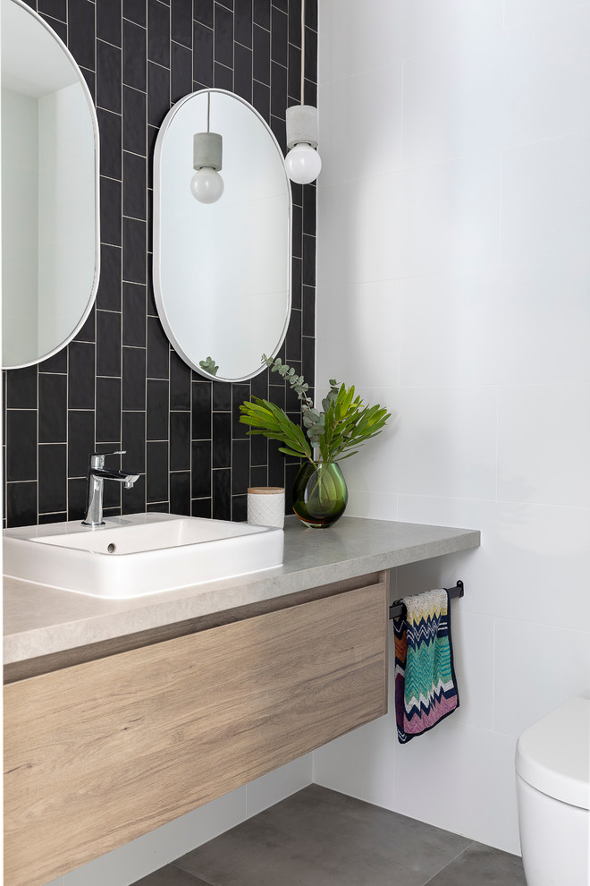 Inspiration for a mid-sized contemporary powder room in Brisbane with medium wood cabinets, a one-piece toilet, black and white tile, ceramic tile, white walls, cement tiles, engineered quartz benchtops, grey floor, grey benchtops, flat-panel cabinets and a drop-in sink.