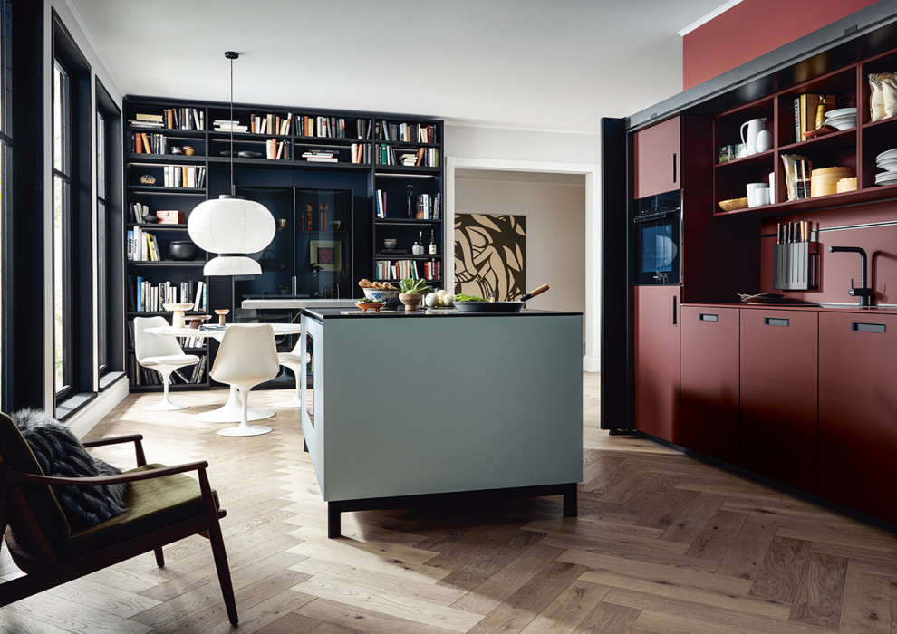 This is an example of a large asian l-shaped open plan kitchen in Nuremberg with flat-panel cabinets, black cabinets, red splashback, black appliances, with island and white benchtop.