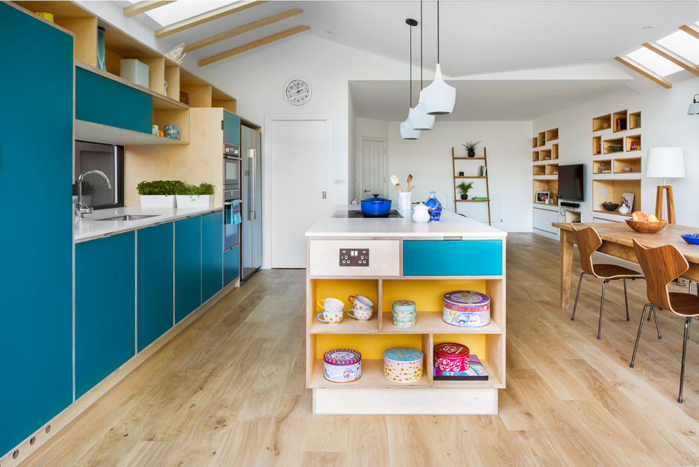 Scandinavian open plan kitchen in London with an undermount sink, flat-panel cabinets, turquoise cabinets, window splashback, light hardwood floors, with island, beige floor and white benchtop.