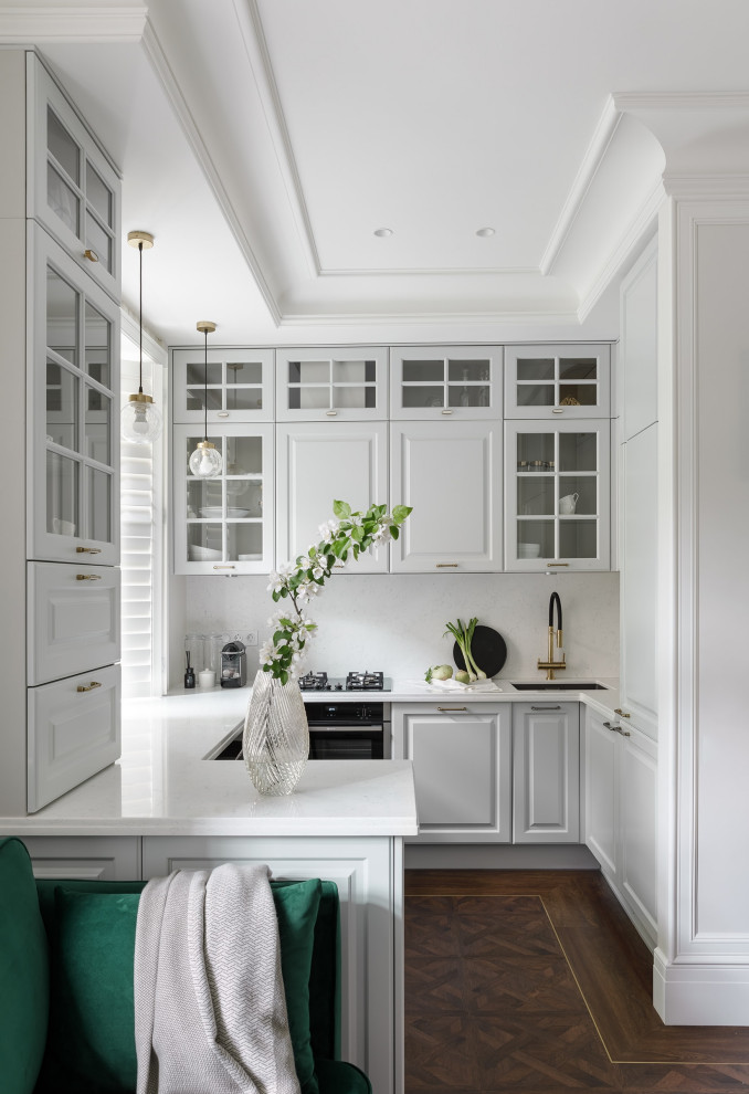 This is an example of a mid-sized scandinavian u-shaped open plan kitchen in Saint Petersburg with an undermount sink, grey cabinets, quartz benchtops, white splashback, engineered quartz splashback, black appliances, vinyl floors, a peninsula, brown floor, white benchtop and raised-panel cabinets.