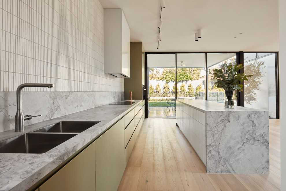 Inspiration for a large contemporary galley eat-in kitchen in Melbourne with a drop-in sink, flat-panel cabinets, green cabinets, marble benchtops, white splashback, ceramic splashback, stainless steel appliances, light hardwood floors, with island, beige floor and white benchtop.