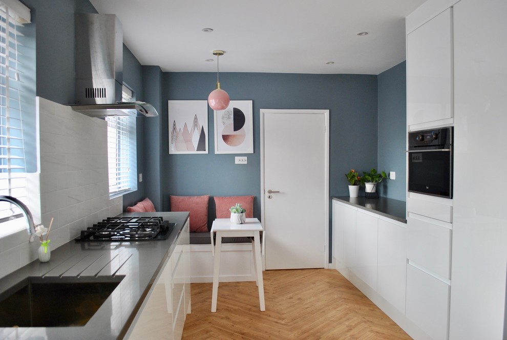 This is an example of a mid-sized modern galley eat-in kitchen in Hertfordshire with a drop-in sink, flat-panel cabinets, white cabinets, white splashback, porcelain splashback, panelled appliances and grey benchtop.