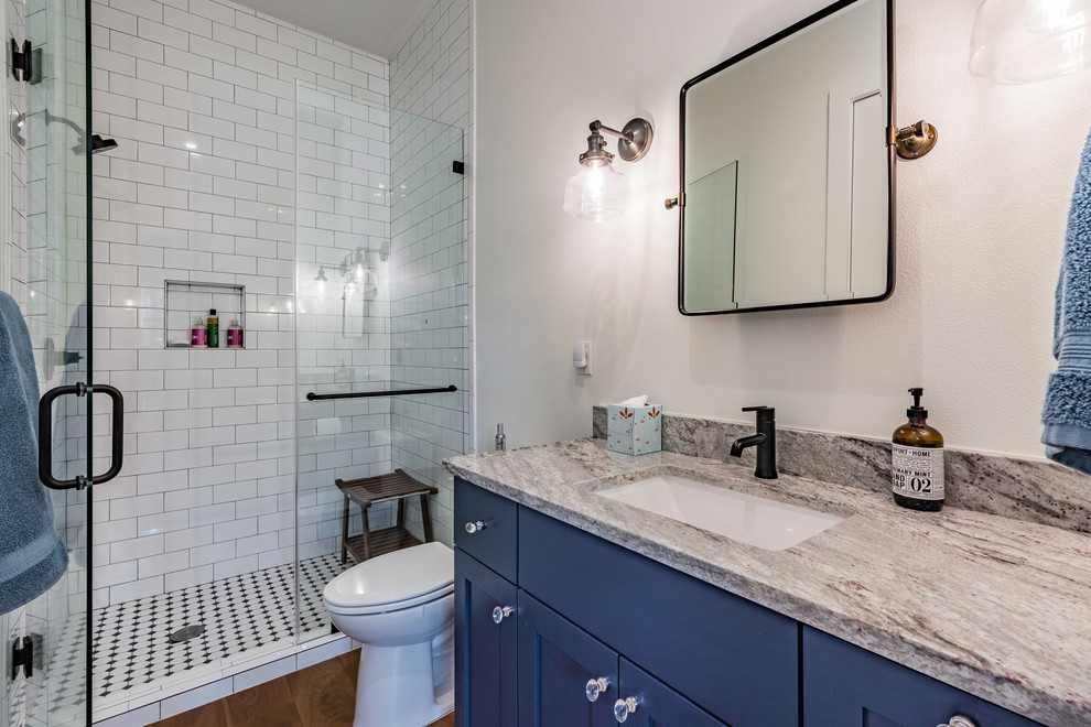 Inspiration for a mid-sized country kids bathroom in Austin with shaker cabinets, blue cabinets, an open shower, white tile, ceramic tile, white walls, medium hardwood floors, an undermount sink, granite benchtops, brown floor, a hinged shower door and multi-coloured benchtops.
