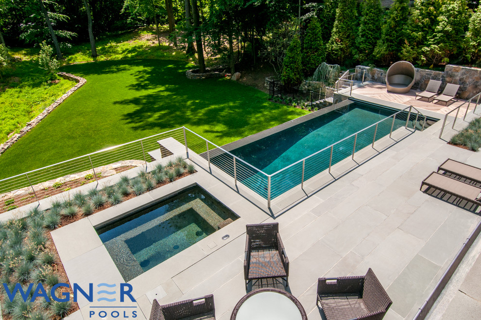 This is an example of a large traditional backyard rectangular infinity pool in New York with a water feature and natural stone pavers.