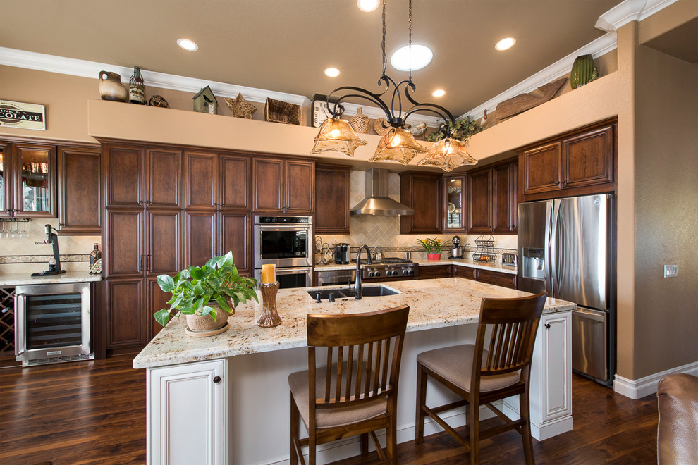 Inspiration for a large traditional l-shaped open plan kitchen in Orange County with a double-bowl sink, recessed-panel cabinets, dark wood cabinets, granite benchtops, beige splashback, stone tile splashback, stainless steel appliances, medium hardwood floors and with island.