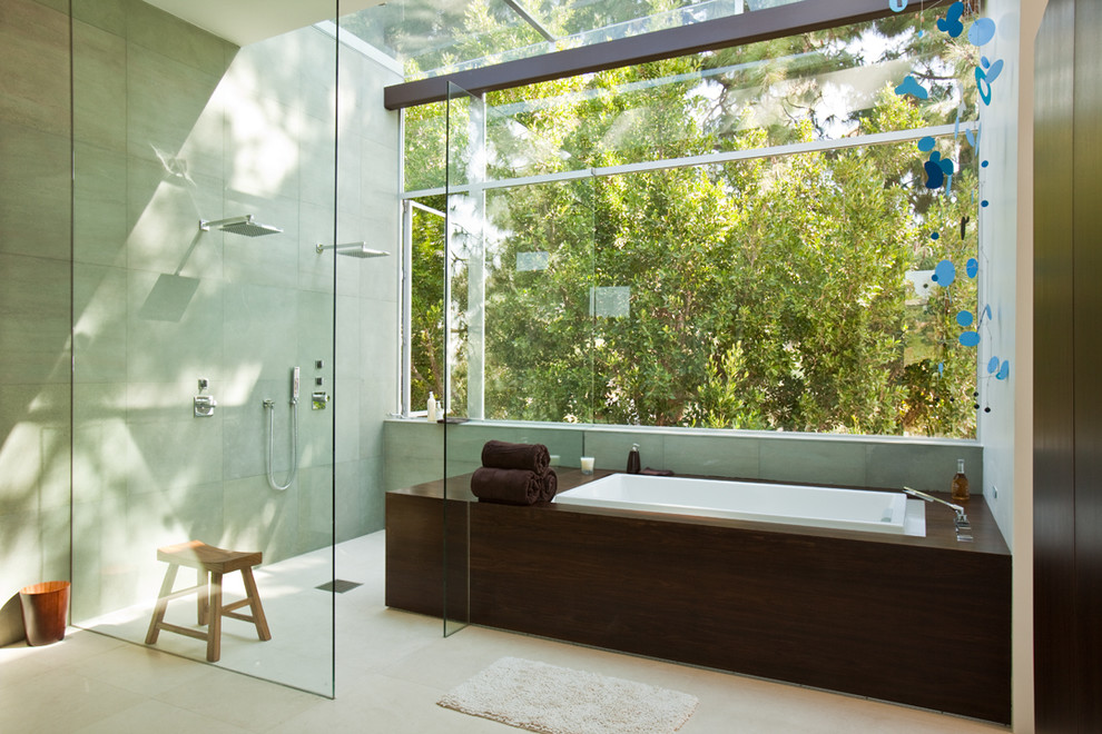 Design ideas for a mid-sized midcentury master bathroom in Los Angeles with a drop-in sink, flat-panel cabinets, dark wood cabinets, solid surface benchtops, a drop-in tub, a curbless shower, a one-piece toilet, green tile, stone tile, white walls and limestone floors.