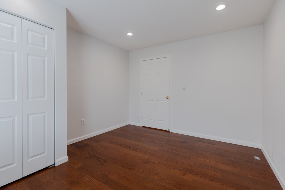 Cette photo montre une chambre parentale moderne de taille moyenne avec un mur blanc, un sol marron, un mur en parement de brique, une cheminée d'angle, un manteau de cheminée en carrelage et parquet foncé.