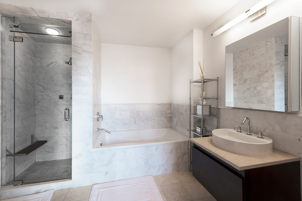 Photo of a mid-sized modern master bathroom in New York with glass-front cabinets, grey cabinets, a drop-in tub, an open shower, a two-piece toilet, white tile, porcelain tile, white walls, marble floors, a drop-in sink and marble benchtops.