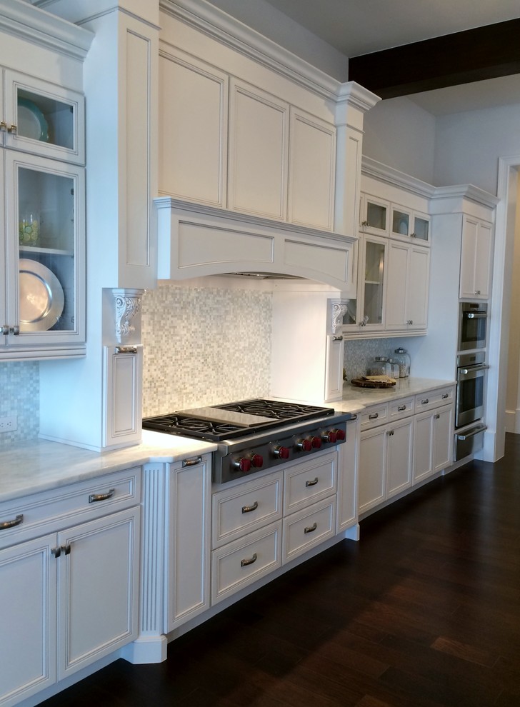 Example of a large transitional galley dark wood floor eat-in kitchen design in Tampa with a farmhouse sink, recessed-panel cabinets, white cabinets, marble countertops, white backsplash, glass tile backsplash, paneled appliances and an island