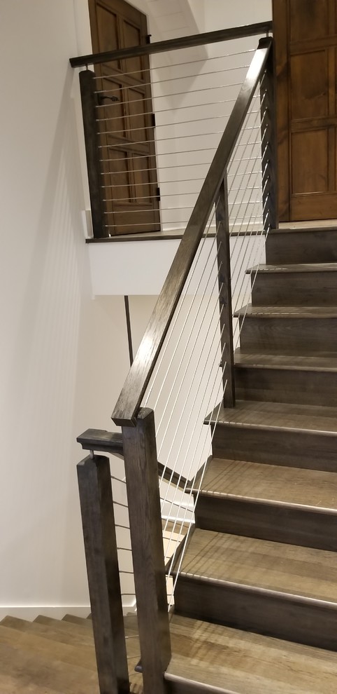 Large country wood u-shaped staircase with wood risers and cable railing.