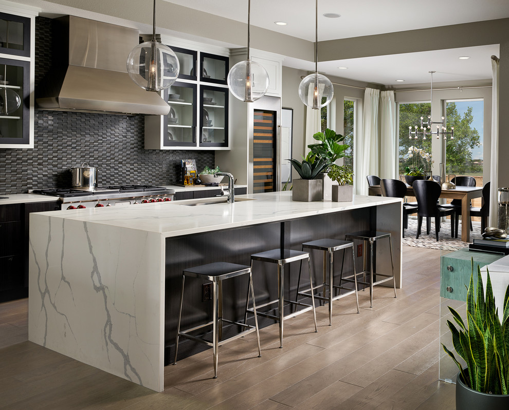 This is an example of a contemporary galley eat-in kitchen in Denver with an undermount sink, glass-front cabinets, black cabinets, black splashback, mosaic tile splashback, stainless steel appliances, light hardwood floors, with island, beige floor and white benchtop.