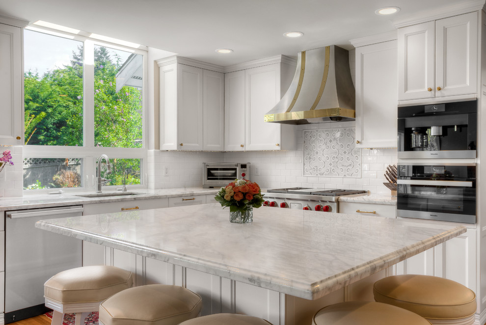 This is an example of a mid-sized transitional l-shaped open plan kitchen in Seattle with an undermount sink, flat-panel cabinets, white cabinets, marble benchtops, white splashback, subway tile splashback, stainless steel appliances and with island.