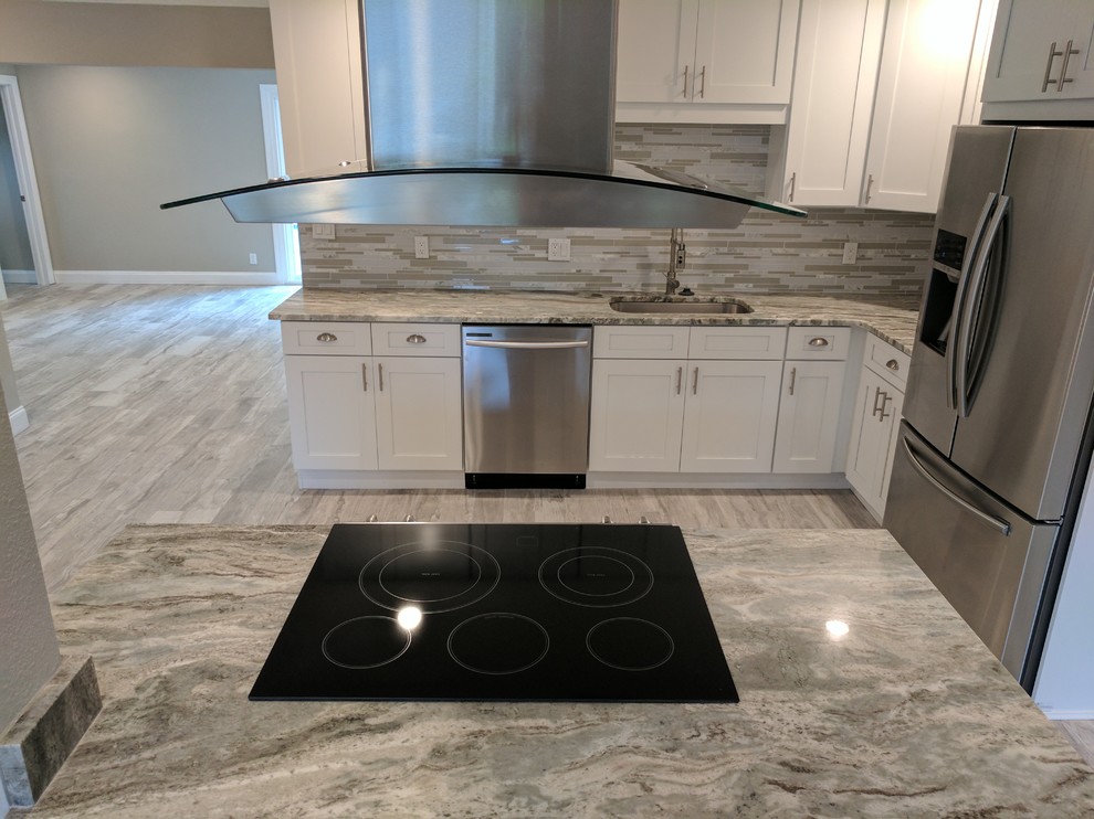 Mid-sized transitional l-shaped light wood floor and gray floor enclosed kitchen photo with an undermount sink, shaker cabinets, white cabinets, granite countertops, multicolored backsplash, matchstick tile backsplash, stainless steel appliances, no island and gray countertops