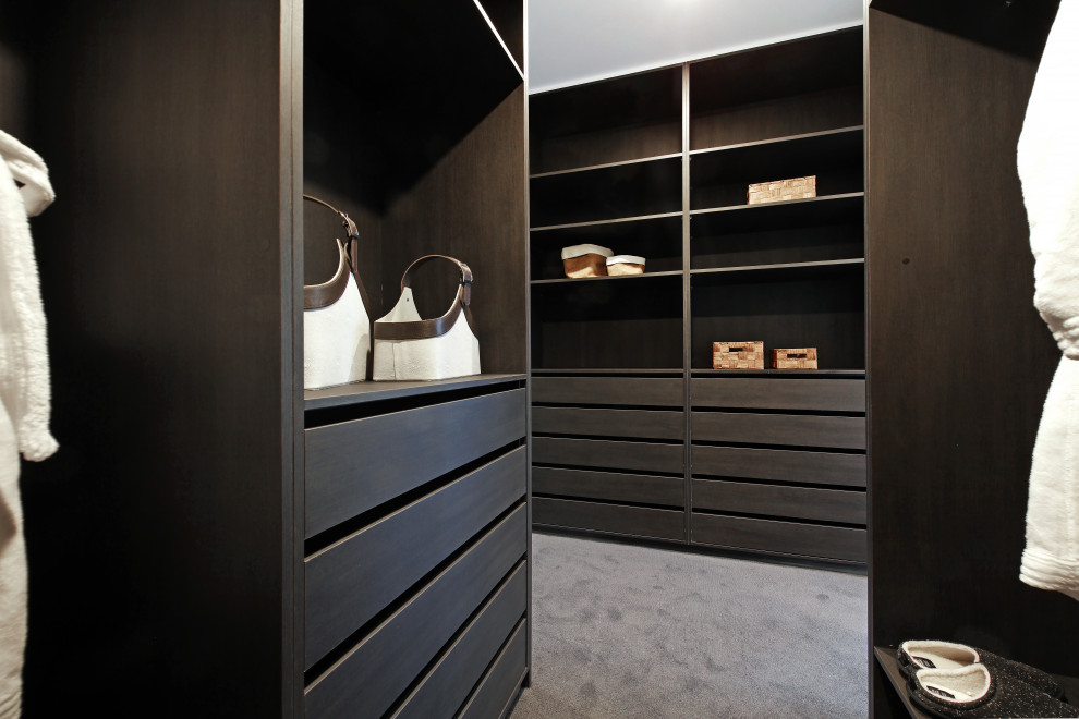This is an example of an expansive contemporary gender-neutral walk-in wardrobe in Melbourne with flat-panel cabinets, dark wood cabinets, carpet and beige floor.