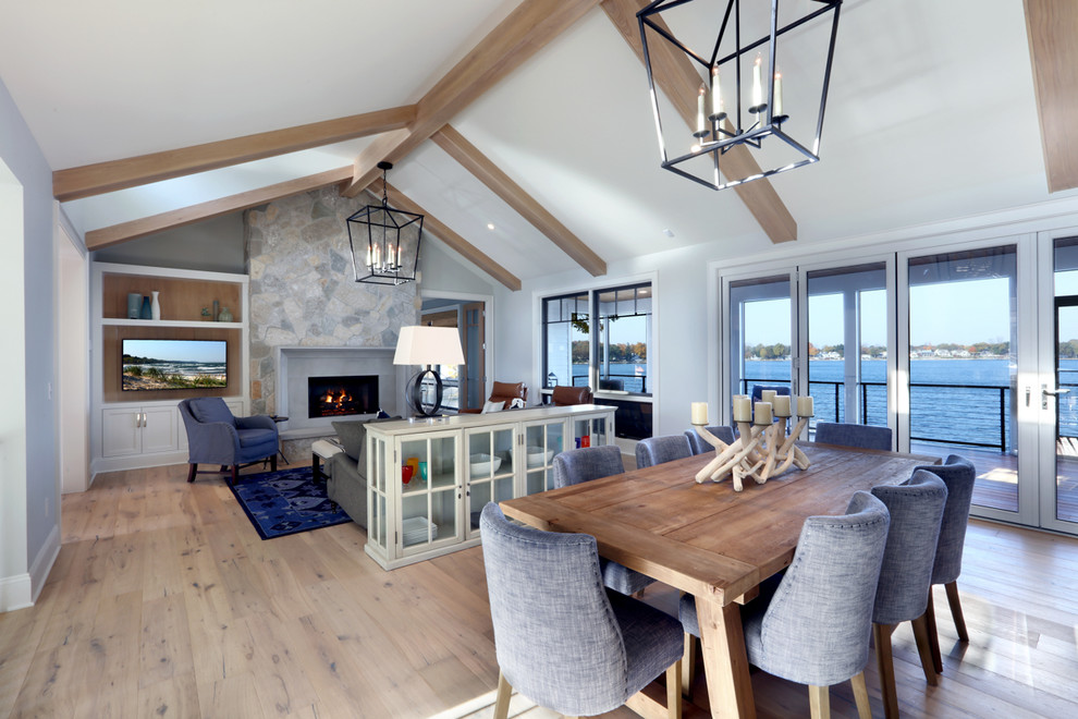 This is an example of an expansive beach style open concept family room in Grand Rapids with light hardwood floors, a standard fireplace, a stone fireplace surround and grey walls.