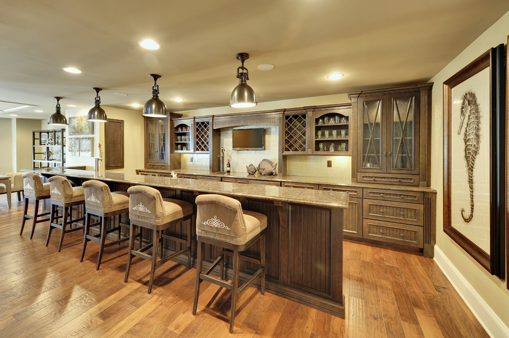 This is an example of a large traditional galley seated home bar in Philadelphia with medium hardwood floors, recessed-panel cabinets, dark wood cabinets, beige splashback and brown floor.