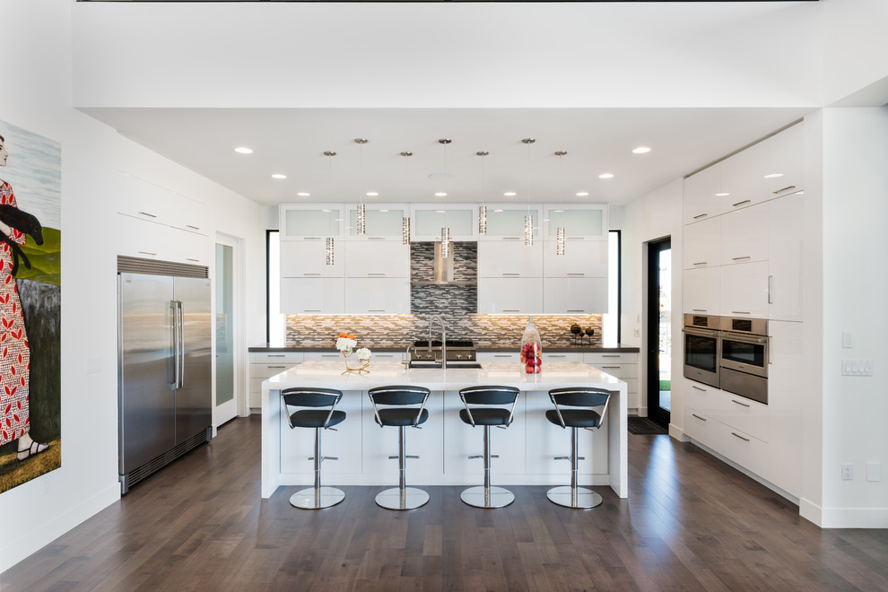 Design ideas for a contemporary u-shaped kitchen in Salt Lake City with an undermount sink, flat-panel cabinets, white cabinets, grey splashback, matchstick tile splashback, stainless steel appliances, medium hardwood floors, with island and brown floor.
