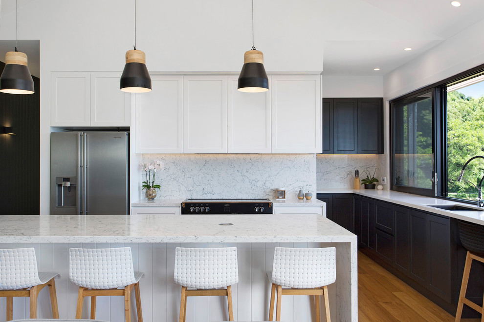 Inspiration for a contemporary l-shaped eat-in kitchen in Wollongong with with island, a double-bowl sink, shaker cabinets, black cabinets, white splashback, stainless steel appliances, medium hardwood floors, brown floor and white benchtop.