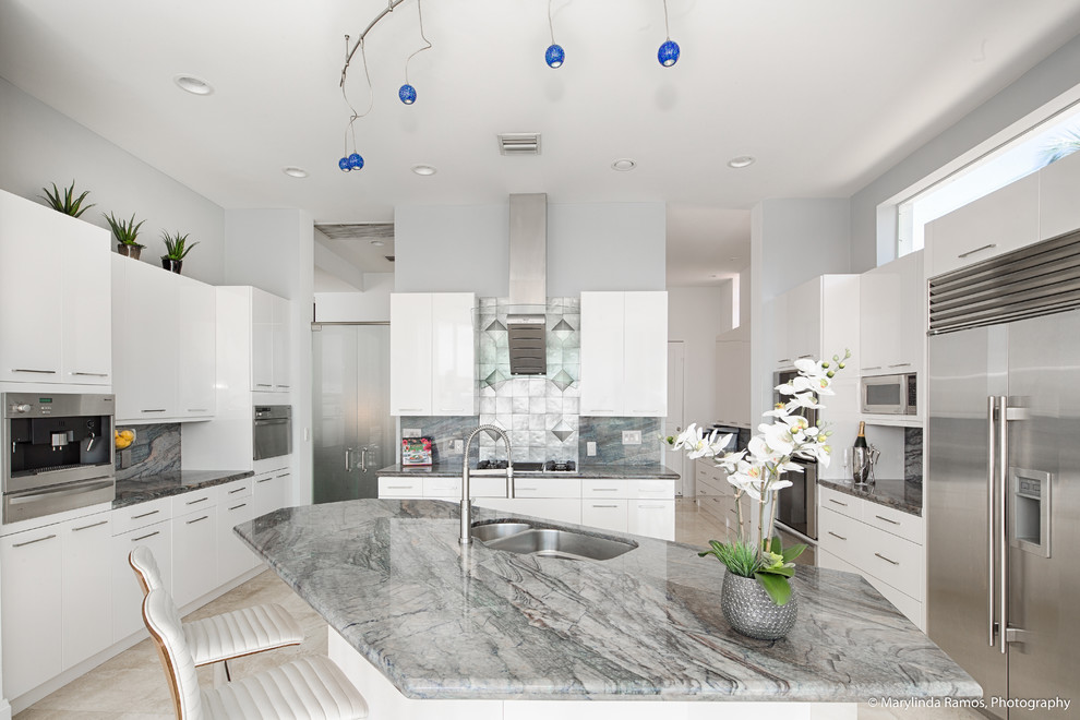 Beach style u-shaped kitchen pantry in Boston with flat-panel cabinets, white cabinets, granite benchtops, grey splashback, metal splashback, stainless steel appliances, cement tiles, with island and beige floor.