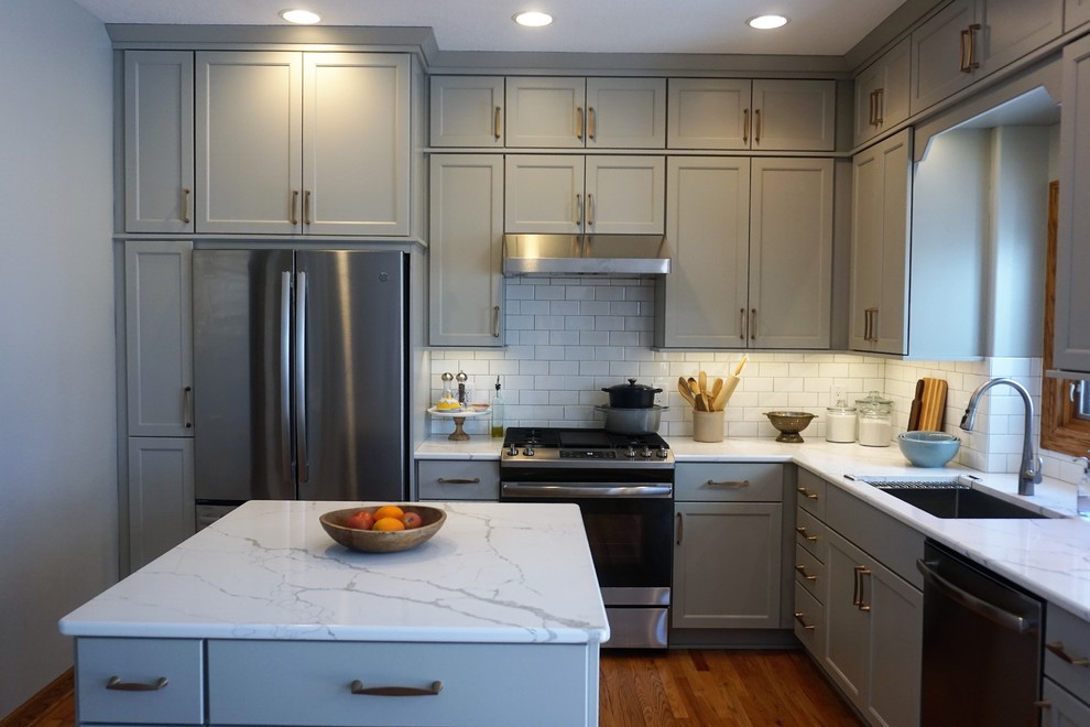 Eat-in kitchen - transitional l-shaped medium tone wood floor eat-in kitchen idea with an undermount sink, recessed-panel cabinets, gray cabinets, quartz countertops, white backsplash, ceramic backsplash, stainless steel appliances, an island and white countertops