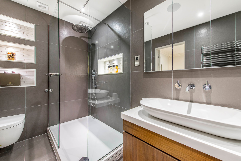 Contemporary 3/4 bathroom in London with flat-panel cabinets, light wood cabinets, a corner shower, a wall-mount toilet, gray tile and a vessel sink.