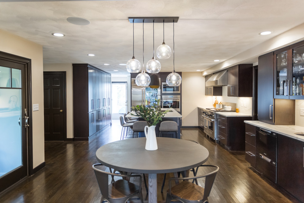 Large contemporary l-shaped eat-in kitchen in Boston with an undermount sink, flat-panel cabinets, black cabinets, solid surface benchtops, white splashback, stone slab splashback, stainless steel appliances, dark hardwood floors, with island, brown floor and white benchtop.