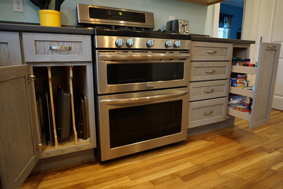 Example of a mid-sized transitional u-shaped medium tone wood floor eat-in kitchen design in Boston with an undermount sink, shaker cabinets, gray cabinets, quartz countertops, black backsplash, stainless steel appliances and an island