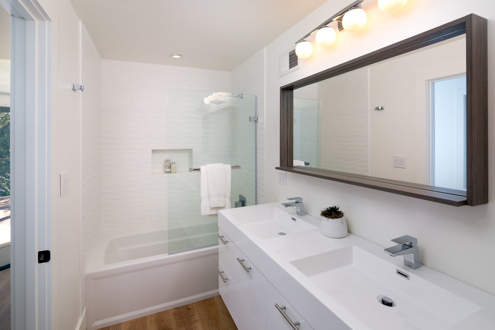 Photo of a mid-sized midcentury 3/4 bathroom in San Francisco with flat-panel cabinets, white cabinets, an alcove tub, a shower/bathtub combo, a one-piece toilet, white tile, ceramic tile, white walls, light hardwood floors, a wall-mount sink, solid surface benchtops, beige floor and an open shower.