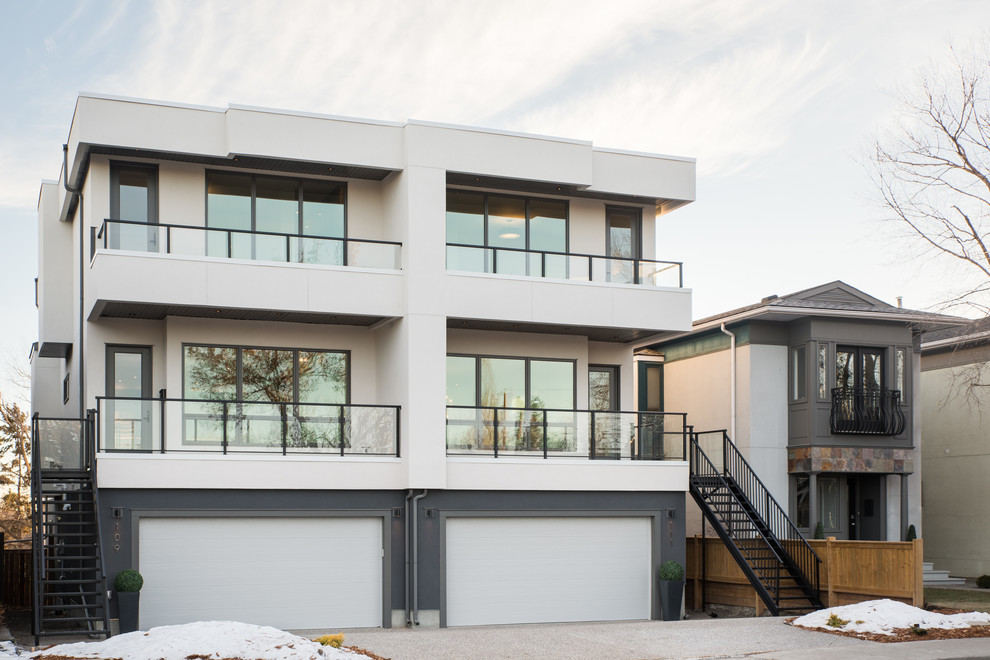 This is an example of a large modern three-storey stucco grey duplex exterior in Calgary.