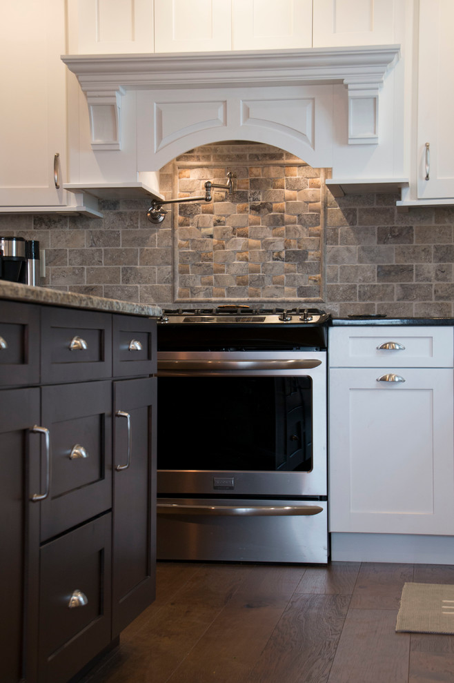 Example of a large transitional l-shaped medium tone wood floor eat-in kitchen design with an undermount sink, shaker cabinets, white cabinets, granite countertops, gray backsplash, stone tile backsplash, stainless steel appliances and an island