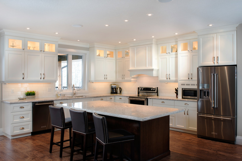 Large transitional l-shaped kitchen in Toronto with an undermount sink, recessed-panel cabinets, white cabinets, quartz benchtops, white splashback, subway tile splashback, stainless steel appliances, medium hardwood floors and with island.