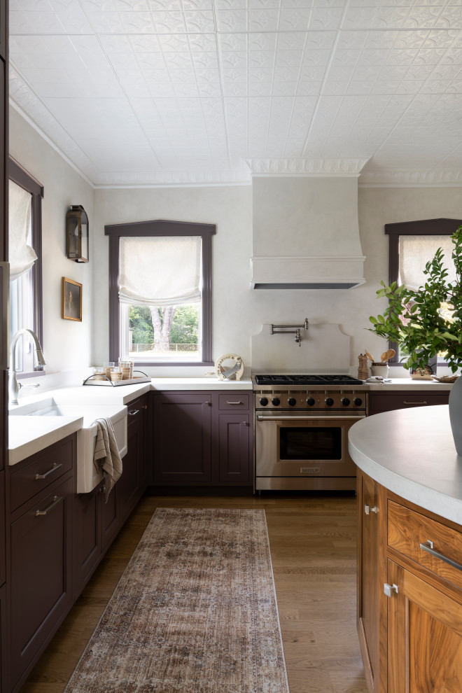 Photo of a mid-sized country l-shaped eat-in kitchen in Newark with a farmhouse sink, beaded inset cabinets, concrete benchtops, panelled appliances, light hardwood floors, with island and beige benchtop.