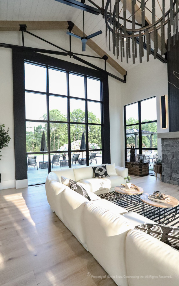 This is an example of an expansive industrial open concept living room in Other with white walls, light hardwood floors, a two-sided fireplace, no tv and vaulted.