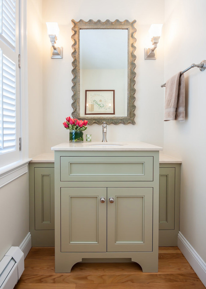 Photo of a traditional powder room in Boston with green cabinets, an undermount sink, recessed-panel cabinets, white walls, medium hardwood floors and white benchtops.